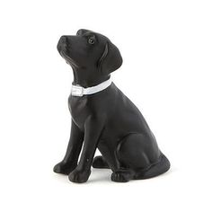 a black dog figurine sitting on the ground with its head turned to the side