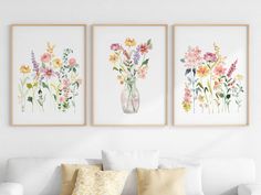 three framed floral prints hang above a white couch