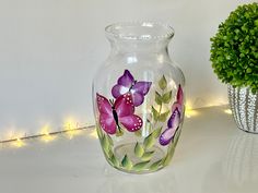 a vase with flowers painted on it next to a potted plant and string lights