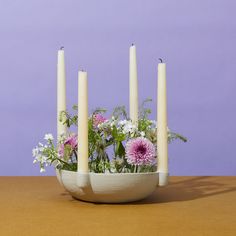 a bowl with flowers and candles in it on a table next to a purple wall