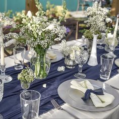 the table is set with white and blue flowers in vases, napkins, and silverware