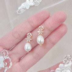 two pairs of pearl and crystal earrings on pink gloves with white flowers in the background