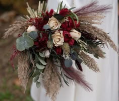 a bridal bouquet with red and white flowers is held by a bride's arm