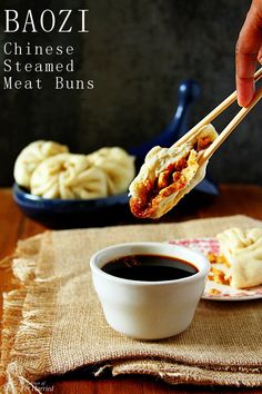 a person holding chopsticks over a plate with meat buns and dipping sauce