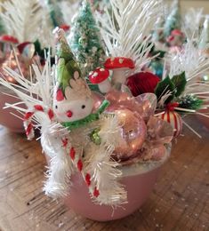 small christmas trees and ornaments in pink pots on a wooden table with white tinsel