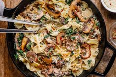 a skillet with pasta, mushrooms and parmesan cheese in it on a wooden table