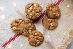 four chocolate chip cookies sitting on top of a white table cloth next to a red and white striped napkin