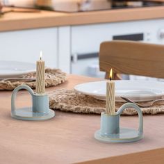 two candles sitting on top of a wooden table next to plates and utensils