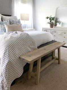 a bed with white sheets and pillows in a bedroom next to a dresser, mirror and lamp