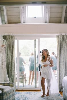 a woman standing in front of a glass door wearing a white dress and looking at the camera