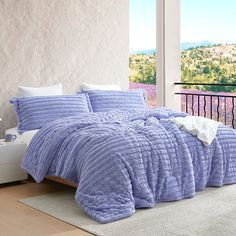 a bed in a room with a purple comforter and pillows on top of it