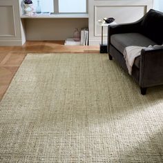 a living room area with a couch, window and rug on the floor in front of it