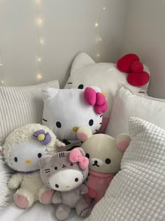 several hello kitty stuffed animals on a bed with white pillows and lights in the background