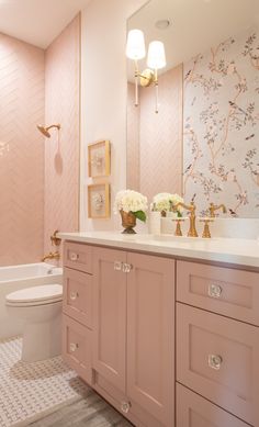 a bathroom with pink cabinets and white toilet next to a bathtub filled with flowers