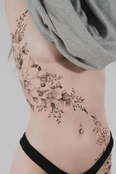 a woman's stomach with flowers and leaves tattooed on her side ribcage