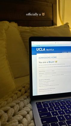 an open laptop computer sitting on top of a bed next to a white blanket and pillows