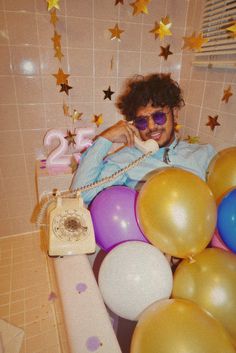 a woman sitting in a bathtub surrounded by balloons and confetti, talking on the phone