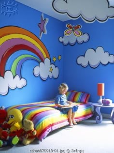 a child sitting on a bed in a room with blue walls and rainbows painted on the wall