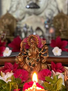 there is a lit candle in front of some flowers and an idol on the table