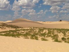 there are many clouds in the sky above sand dunes and green plants on the ground