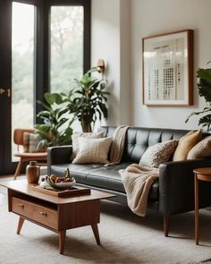 a living room with black leather couches and wooden tables in front of large windows