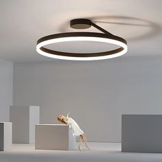 a woman standing on top of a white block in an empty room with a circular light fixture above her head