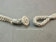 a white rope with a button attached to it on a gray surface next to a pair of scissors