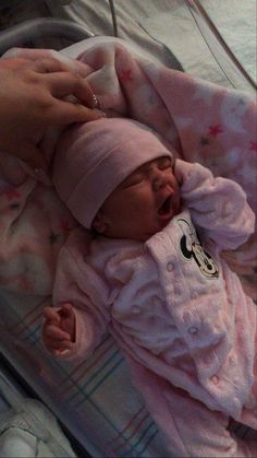 a baby in a pink outfit laying on top of a bed next to a person