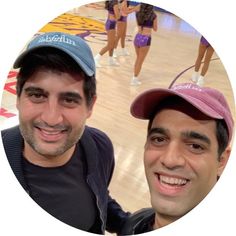 two men standing next to each other in front of a basketball court and smiling at the camera