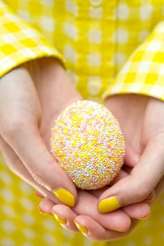 a woman holding a yellow and white sprinkle covered doughnut in her hands