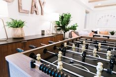 a foosball table in a living room with potted plants on the side