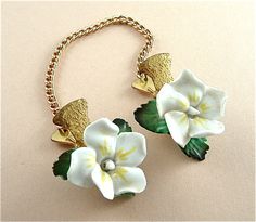 two white flowers with green leaves are attached to a gold chain on a beige surface