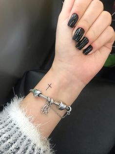 a woman's hand with black nails and a cross tattoo on her left wrist