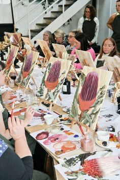 a group of people sitting around a table with paintings on easels in front of them