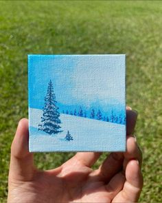 a hand holding up a small piece of paper with a painting of a pine tree on it