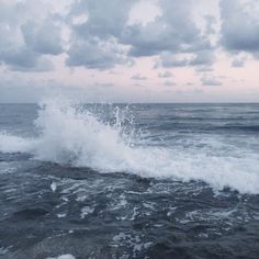 an ocean wave crashing into the shore with dark clouds in the sky over it and water splashing on the rocks