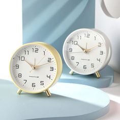 two clocks sitting side by side on a blue and white table with an abstract background