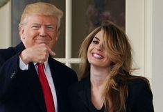 a man and woman standing next to each other in front of a window with one pointing at the camera