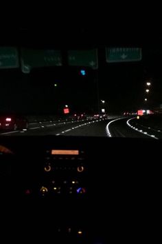 the dashboard of a car at night with lights on and cars driving down the road