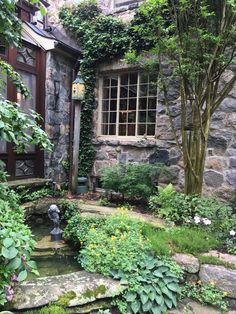 a stone building with lots of greenery around it and a small pond in the middle