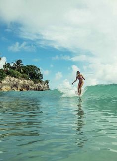 a woman riding a surfboard on top of a wave in the ocean with palm trees behind her