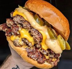 a hand holding a large cheeseburger with pickles and onions on it's bun