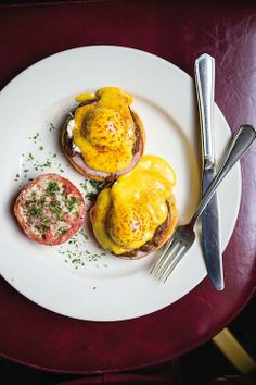 two eggs benedicts on toast with tomato slices and a fork sitting on a white plate