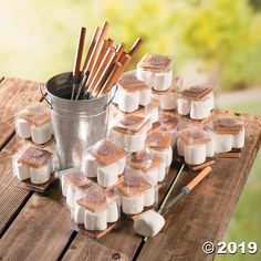 marshmallows are arranged on a picnic table with wooden utensils and an ice bucket