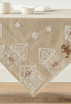 an embroidered tablecloth with gingerbreads and snowflakes is displayed on a wooden floor