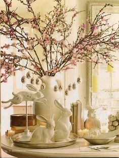 a white vase filled with pink flowers and bunny figurines on top of a table