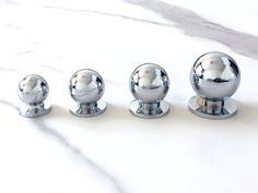 four chrome balls sitting on top of a white counter next to each other in front of a marble surface