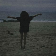 a woman standing on top of a sandy beach next to the ocean at night with her arms outstretched