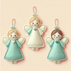 three felt angel ornaments hanging from strings on a pink background, one is blue and the other is white