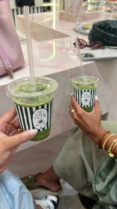 two people holding up green smoothies in their hands